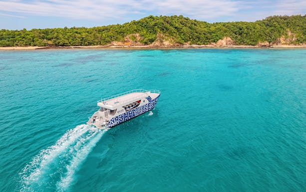Speed boat cruising on turquoise waters near lush green island.