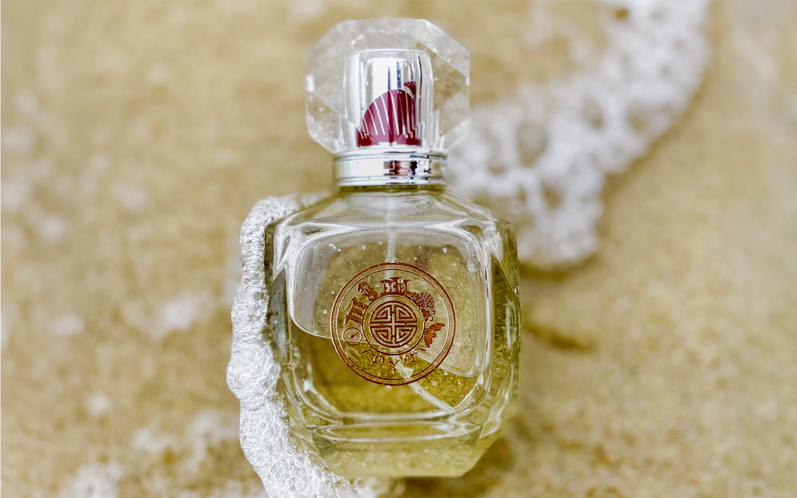 Perfume bottle with ornate design on sandy beach.
