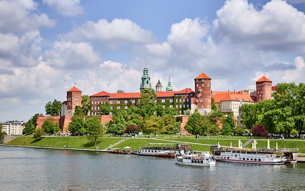 Krakow's Wawel Castle viewed from the Vistula River with sightseeing boats.