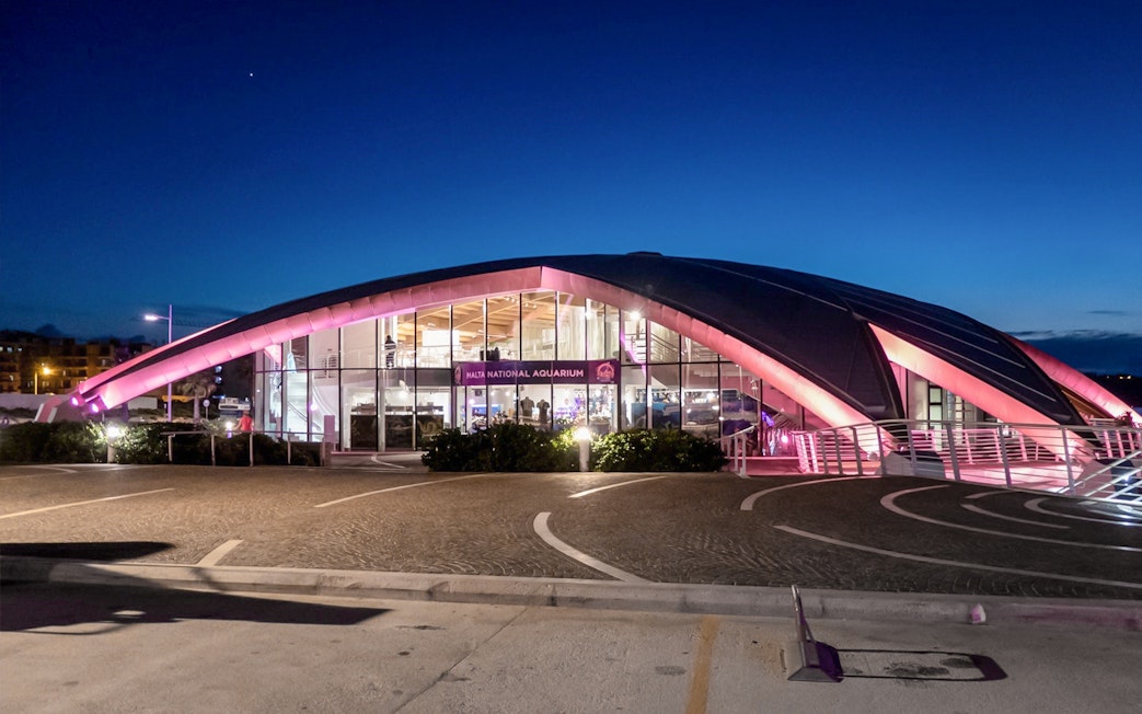 Malta National Aquarium illuminated at dusk with a clear sky.