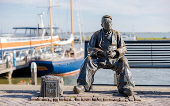 Bronze fisherman statue "De Bap" on Volendam harbor dike with boats in background.