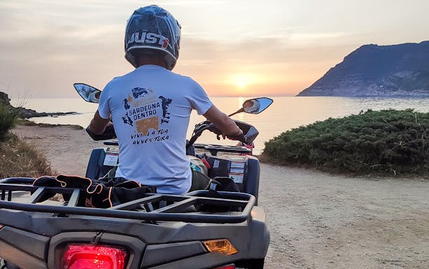Quad bike rider on coastal path at sunset in Alghero, Sardinia.