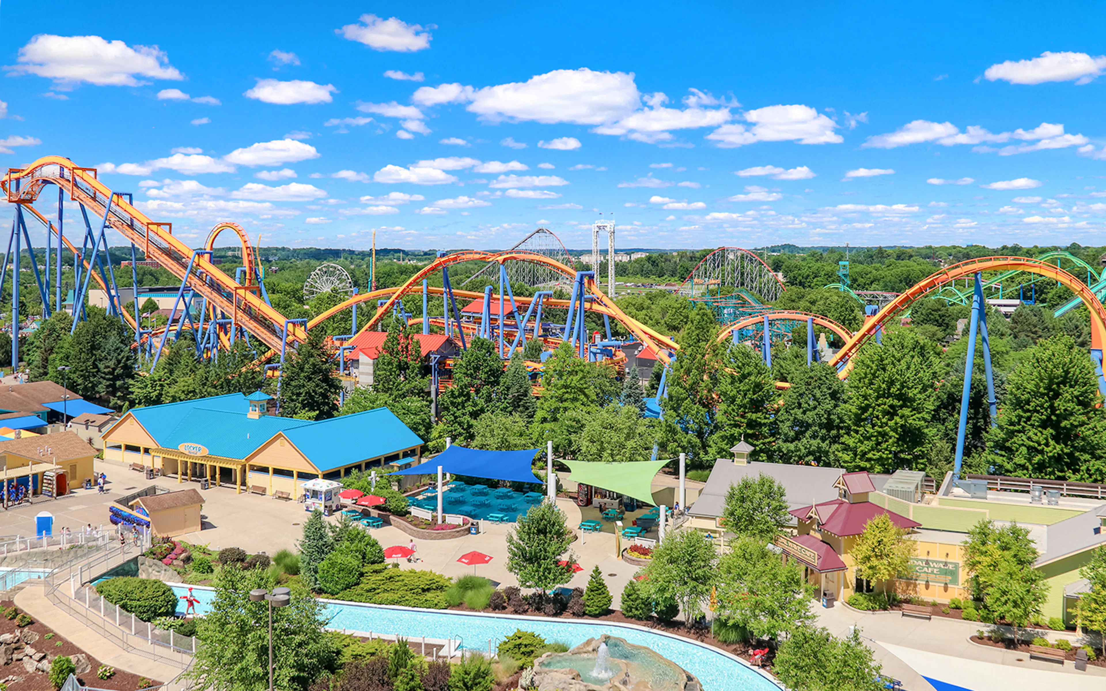 Roller coasters and attractions at Dorney Park, surrounded by lush greenery under a blue sky.