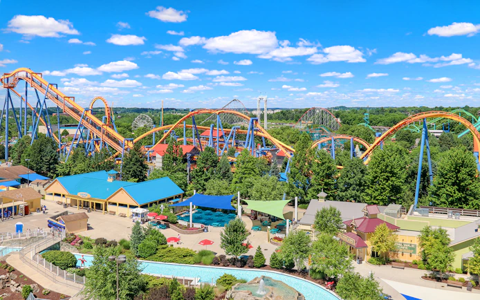 Roller coasters and attractions at Dorney Park, surrounded by lush greenery under a blue sky.
