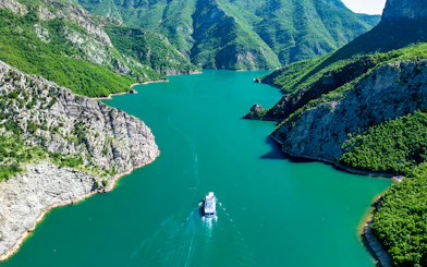 Aerial view of a boat on Komani Lake surrounded by lush mountains in Shkoder, Albania.