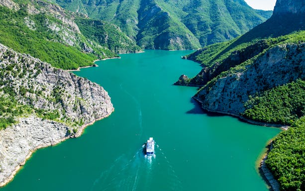 Aerial view of a boat on Komani Lake surrounded by lush mountains in Shkoder, Albania.