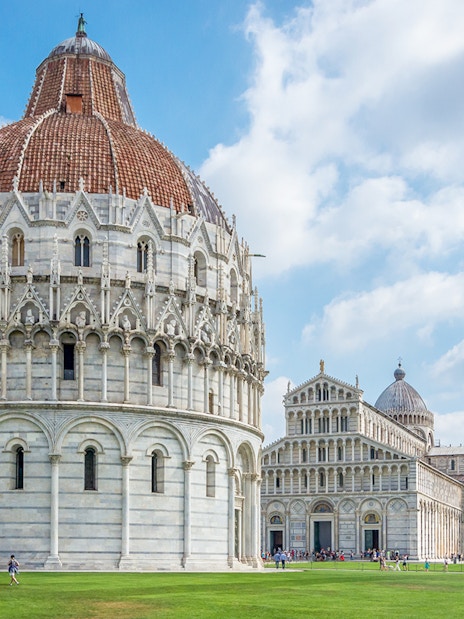Baptistry of San Giovanni exterior with Pisa Cathedral and Leaning Tower in background.