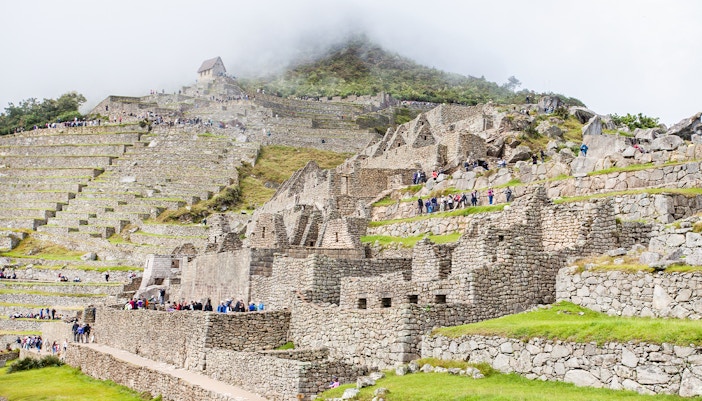 Machu Picchu terraces with stone ruins and tourists exploring the site.