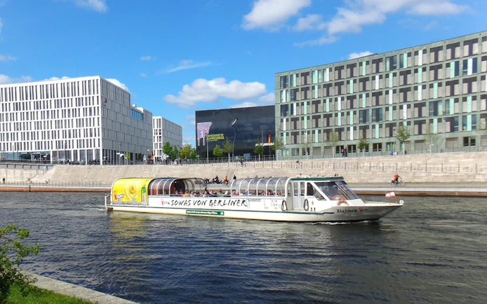 Tour boat cruising on the Spree River in Berlin with modern buildings in the background.