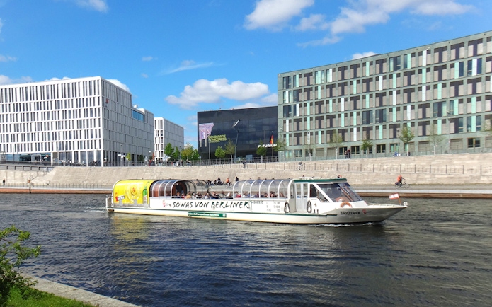 Tour boat cruising on the Spree River in Berlin with modern buildings in the background.