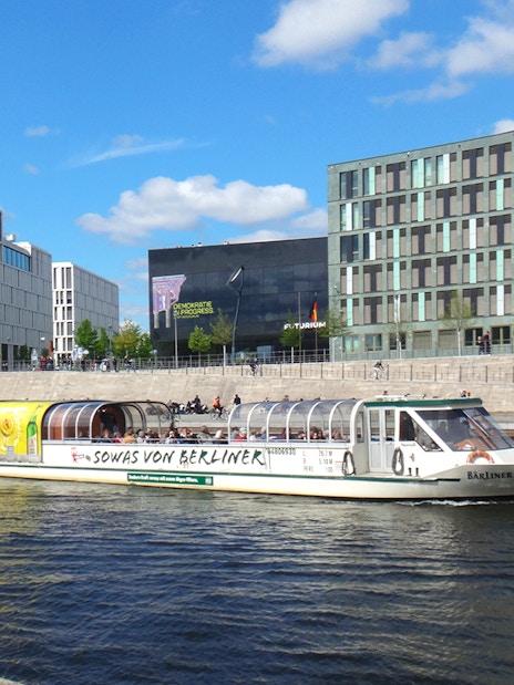 Tour boat cruising on the Spree River in Berlin with modern buildings in the background.
