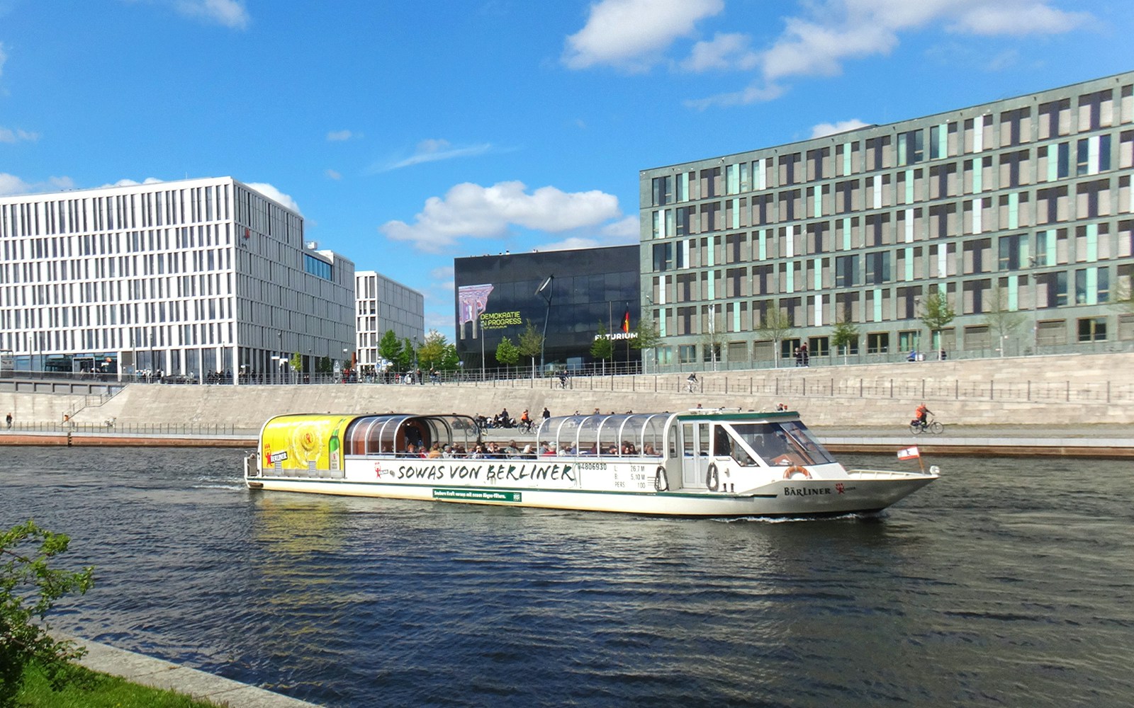 Tour boat cruising on the Spree River in Berlin with modern buildings in the background.