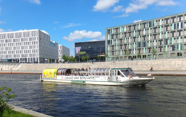 Tour boat cruising on the Spree River in Berlin with modern buildings in the background.