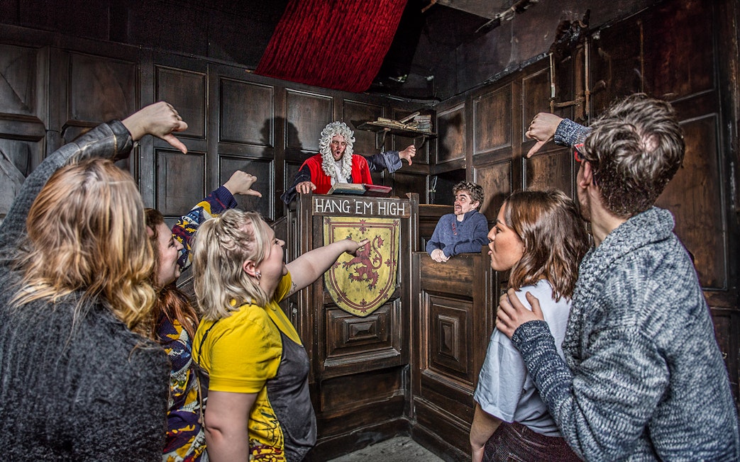 Visitors in The Edinburgh Dungeon Courtroom during a guided tour, interacting with a judge character.