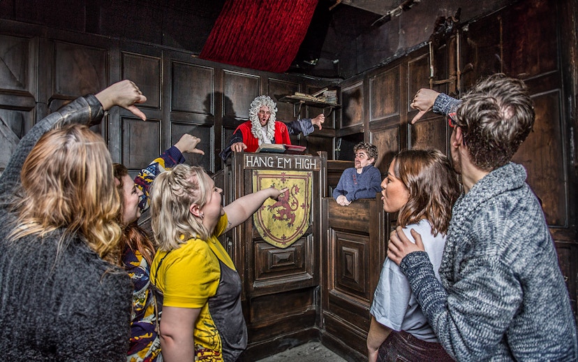 Visitors in The Edinburgh Dungeon Courtroom during a guided tour, interacting with a judge character.