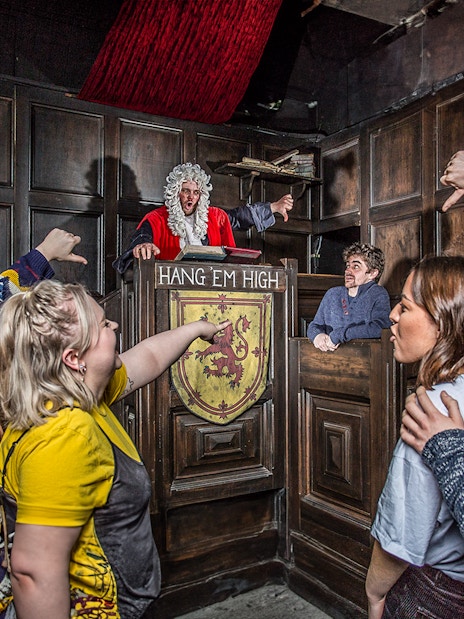Visitors in The Edinburgh Dungeon Courtroom during a guided tour, interacting with a judge character.