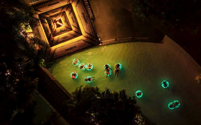 People floating in glowing tubes at night in Siam Park, illuminated water.
