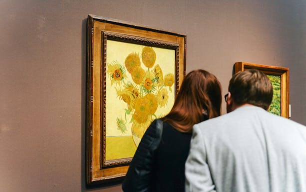 Visitors viewing Van Gogh's Sunflowers painting in a museum.