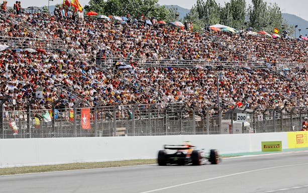 Formula 1 car racing past a packed grandstand at Circuit de Barcelona-Catalunya.