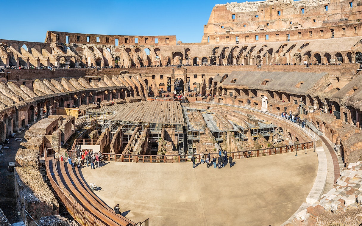 Colosseum interior with tourists exploring ancient amphitheater in Rome, Italy.