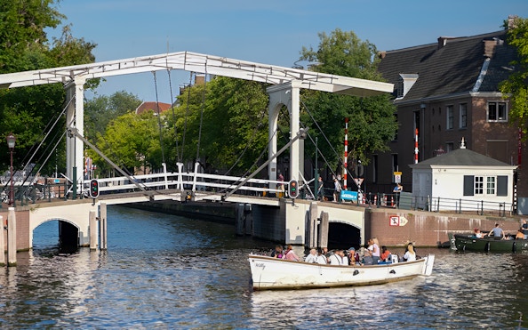 Small open boat cruising under a drawbridge on an Amsterdam canal.