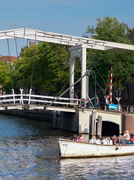 Small open boat cruising under a drawbridge on an Amsterdam canal.