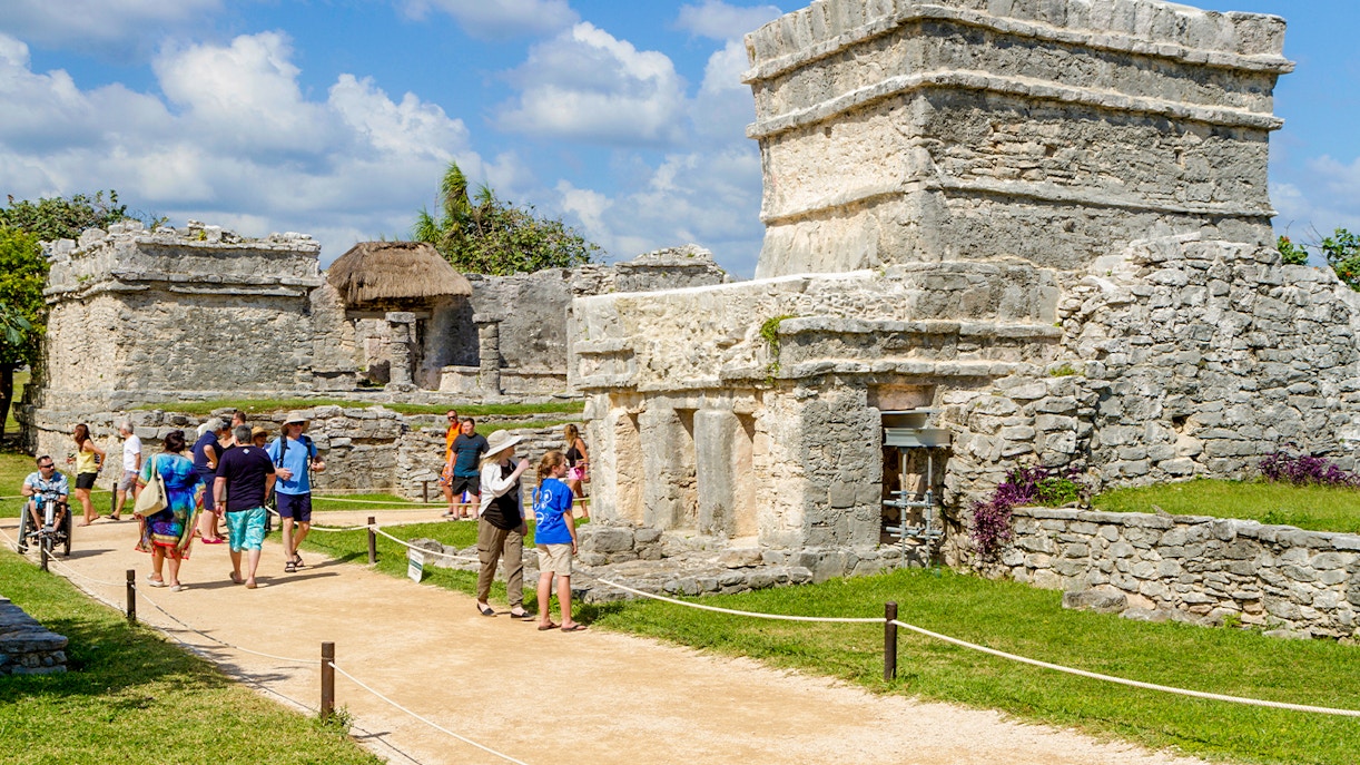 Tourists walking among ancient stone structures at Chichen Itza, Mexico.
