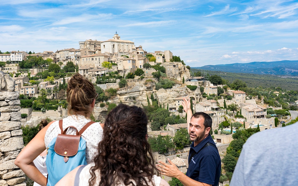 Tour guide explaining the view of Gordes village in Provence to visitors.