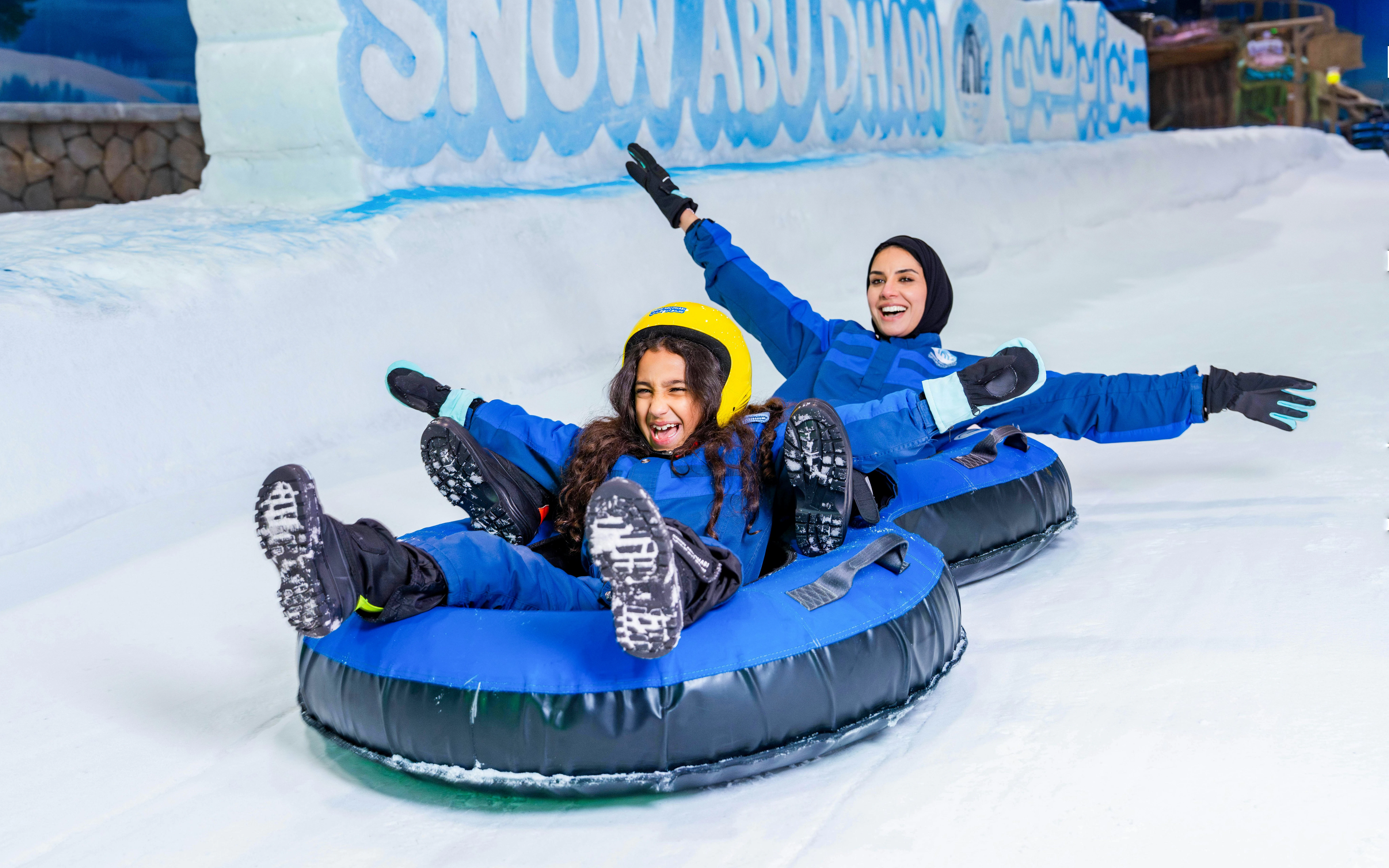 Two people enjoying snow tubing at Snow Abu Dhabi indoor park.
