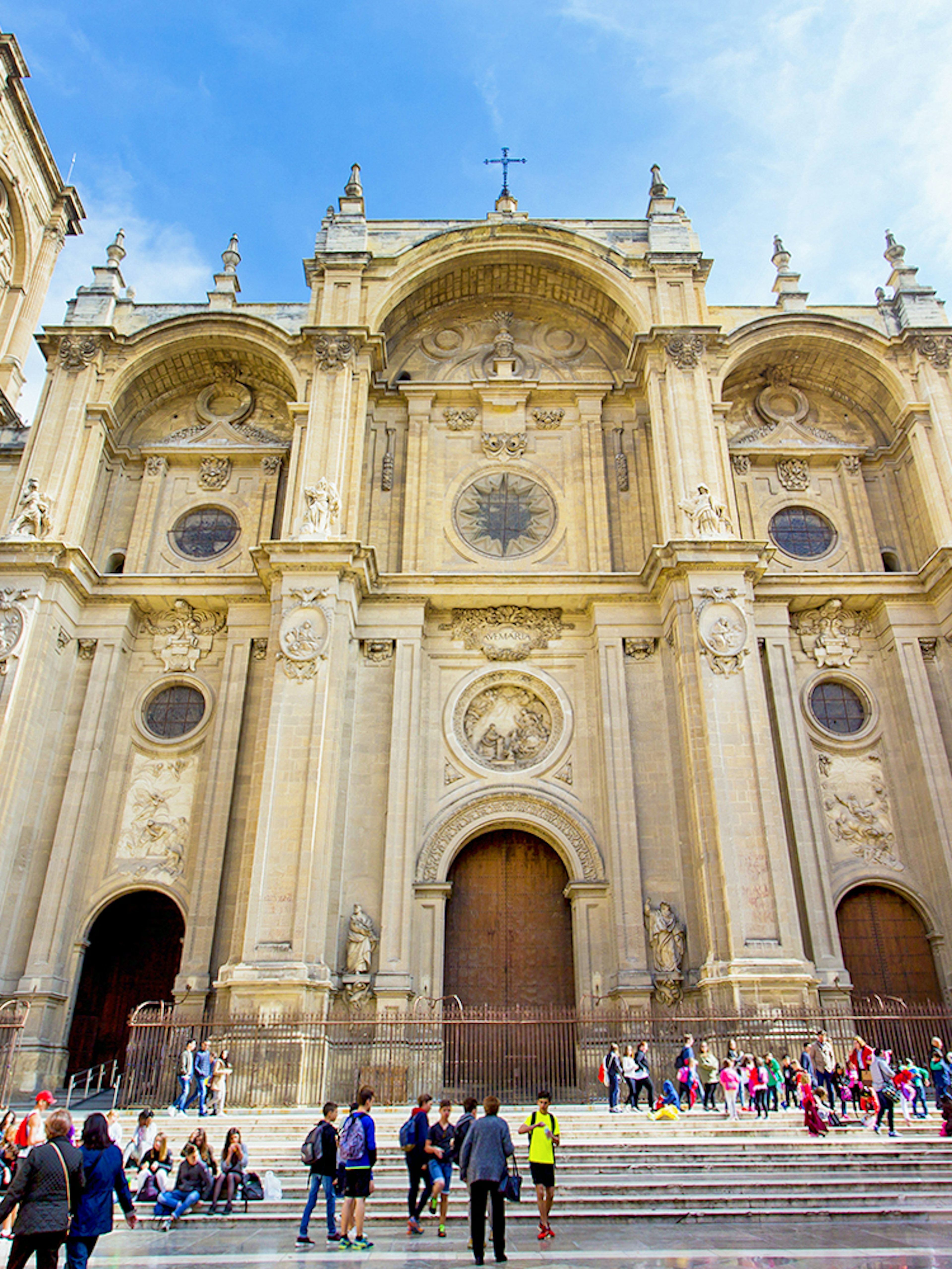 Granada Cathedral facade with visitors on steps, surrounded by historic buildings.
