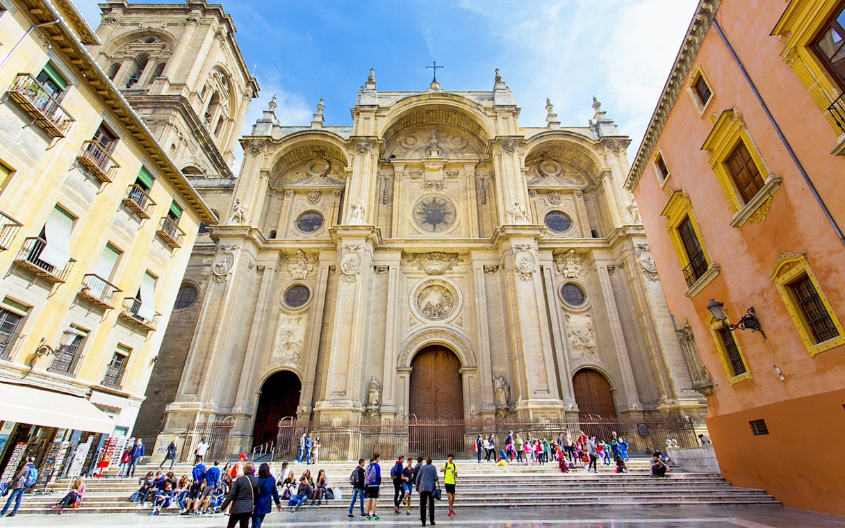 Granada Cathedral facade with visitors on steps, surrounded by historic buildings.