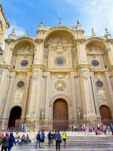 Granada Cathedral facade with visitors on steps, surrounded by historic buildings.