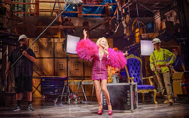 Performer in pink costume on stage with crew, related to "The Queen of Versailles" tour.
