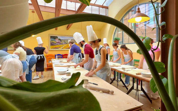 Participants in a cooking class in Siena preparing dough at a long table.