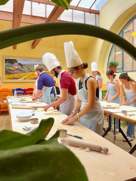 Participants in a cooking class in Siena preparing dough at a long table.