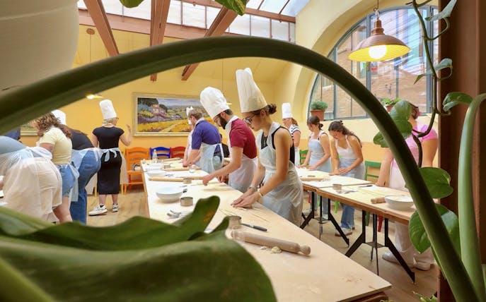 Participants in a cooking class in Siena preparing dough at a long table.