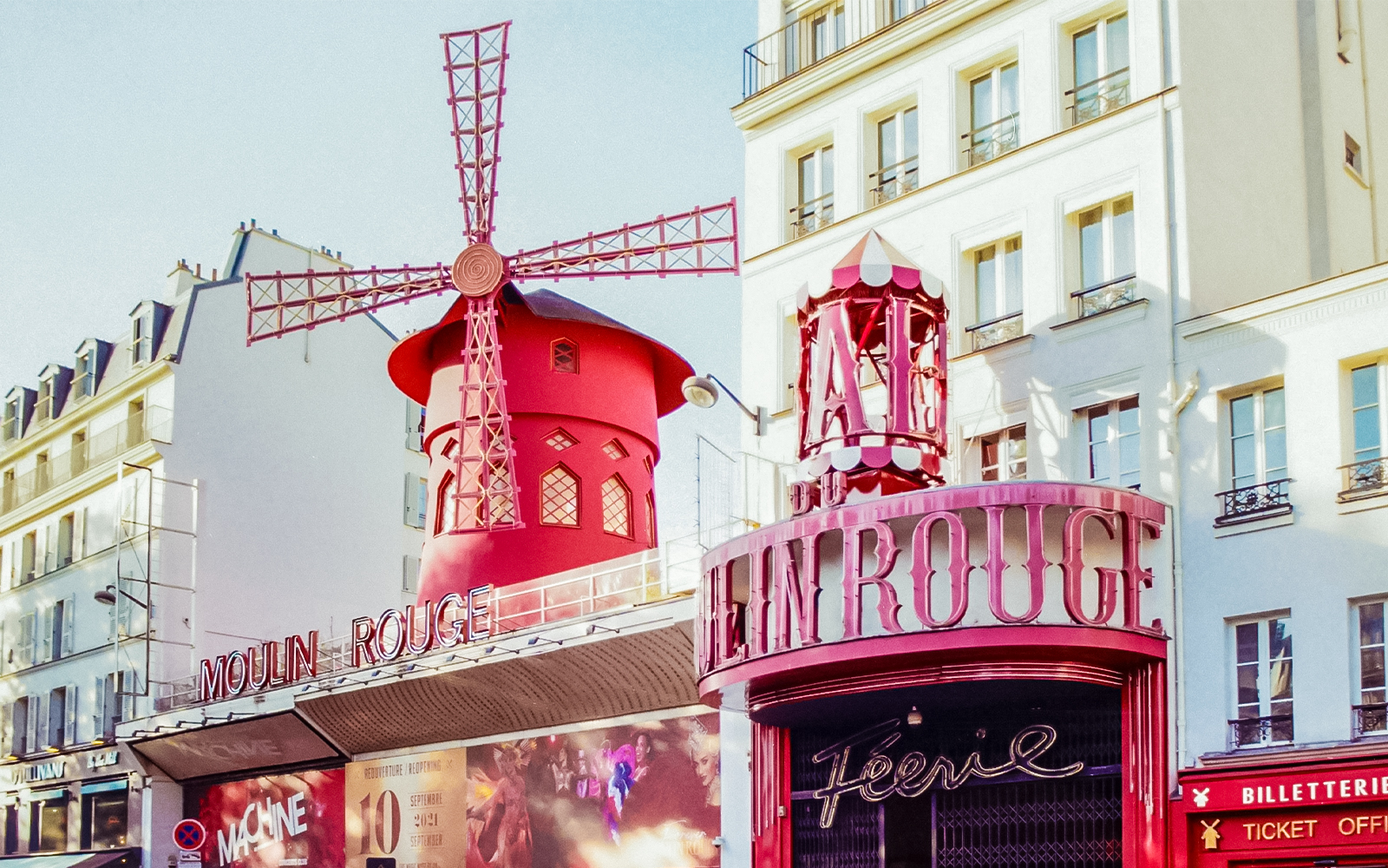 Außenansicht des Moulin Rouge mit roter Windmühle in Paris bei Tageslicht.