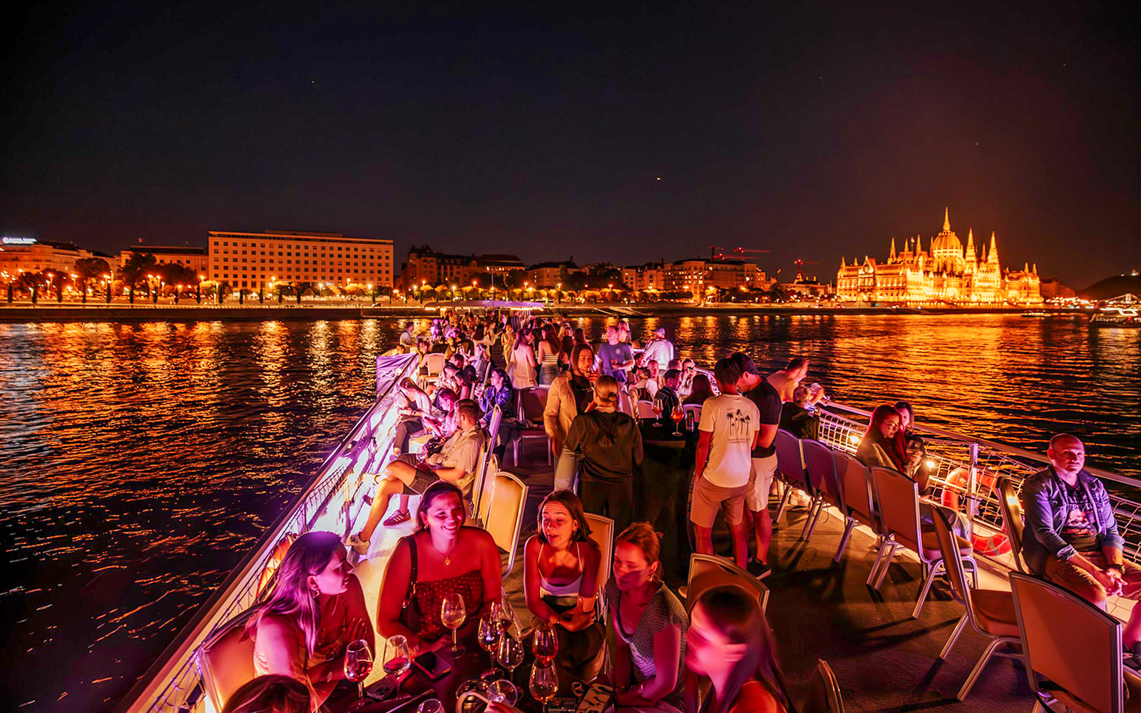 Guests enjoying Budapest Danube River Floating Beerfest with illuminated cityscape.