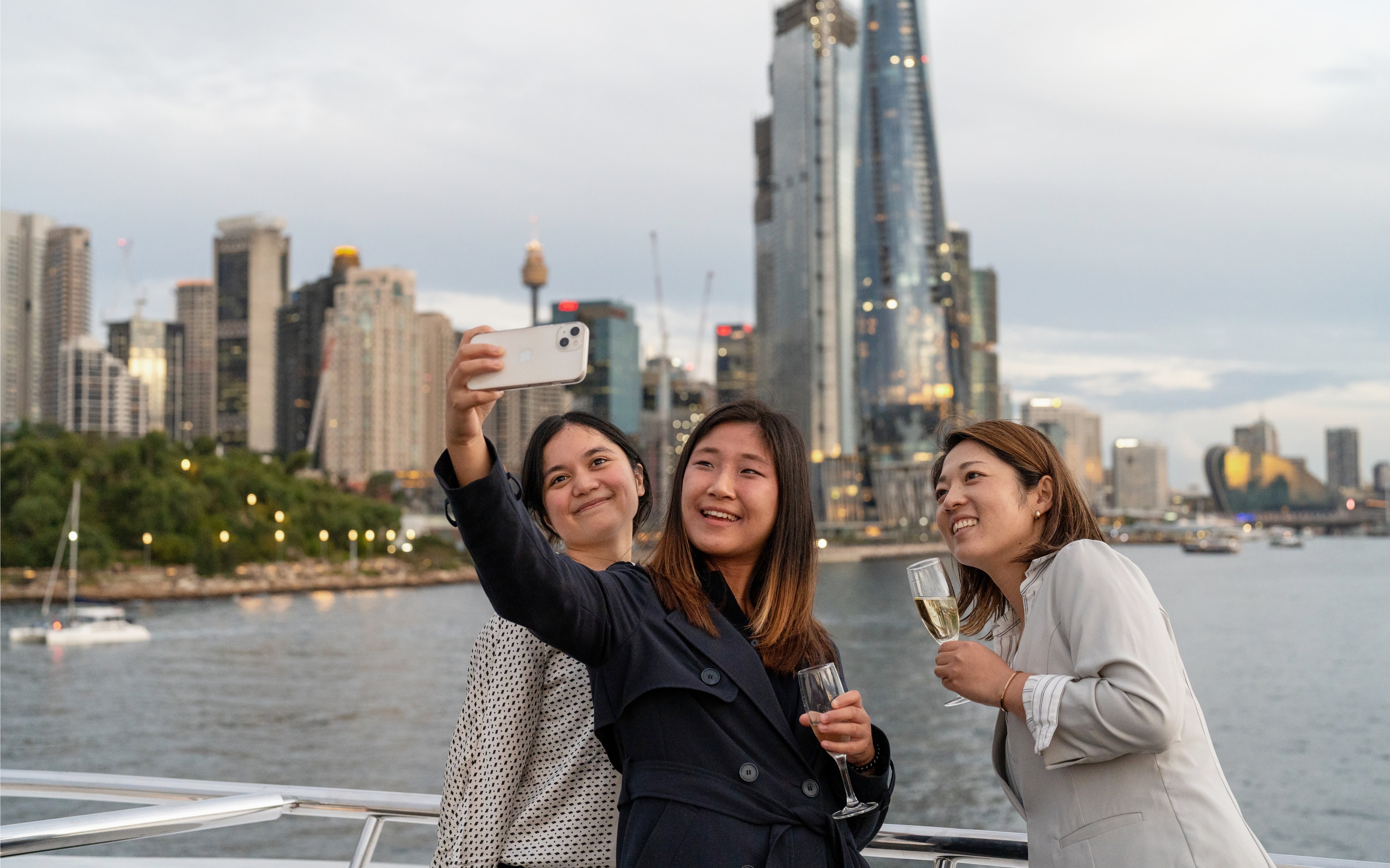 People taking a selfie on a Sydney Harbour cruise with city skyline in the background.