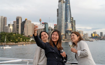 People taking a selfie on a Sydney Harbour cruise with city skyline in the background.