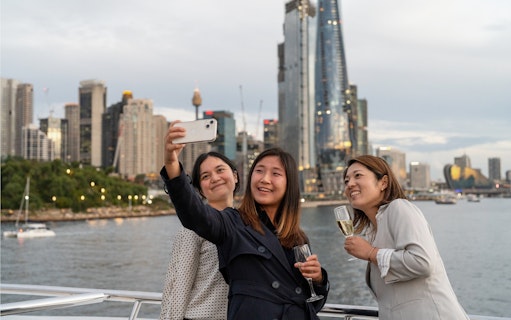 People taking a selfie on a Sydney Harbour cruise with city skyline in the background.