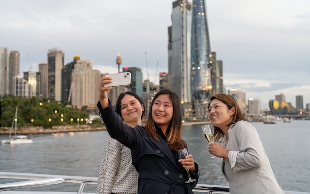 People taking a selfie on a Sydney Harbour cruise with city skyline in the background.