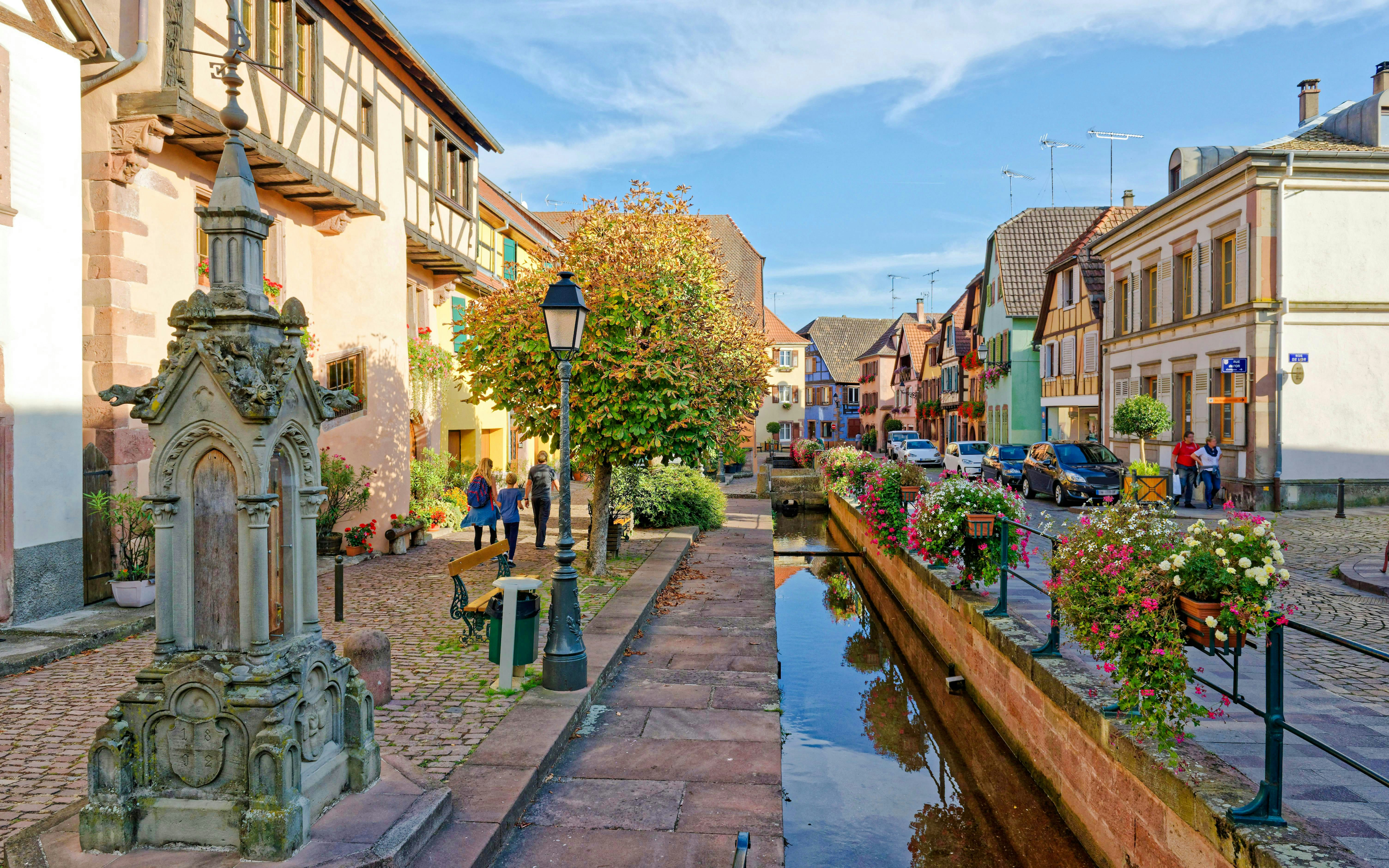 Grand Rue in Alsace with historic buildings, canal, and people walking.