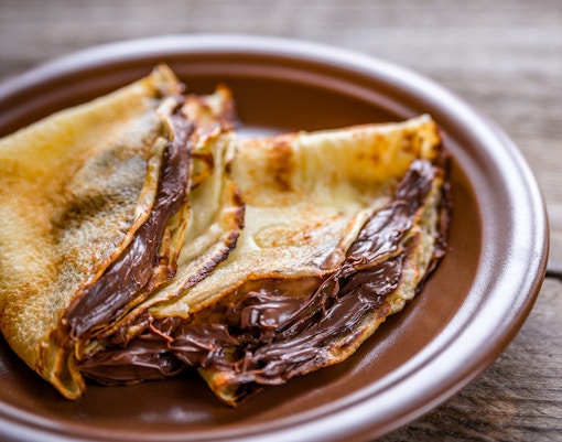 Crepes filled with chocolate cream on a brown plate.