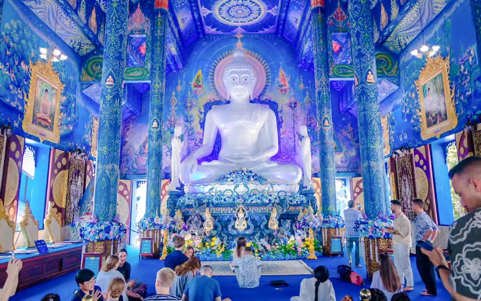 Interior of Blue Temple (Wat Rong Sua Ten) with white Buddha statue and ornate blue decor.