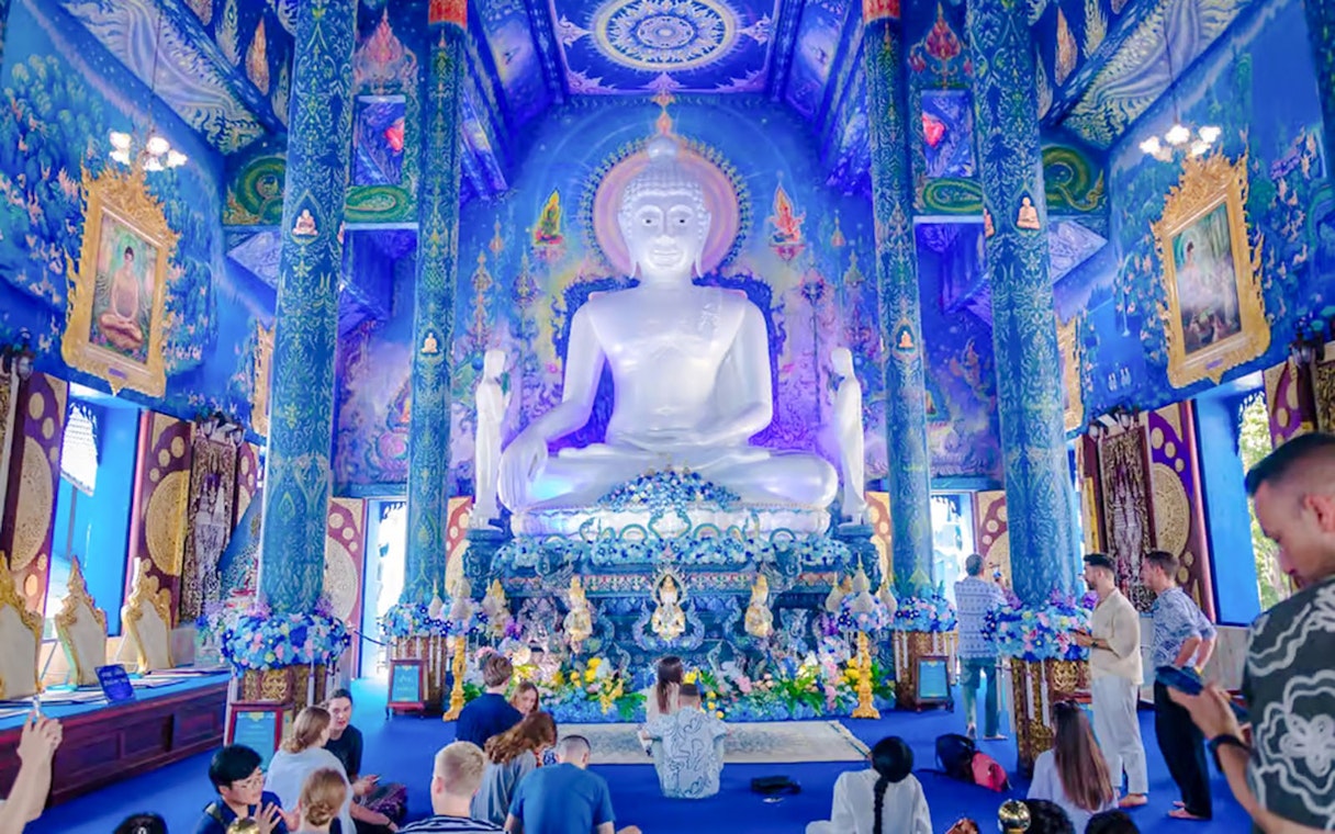Interior of Blue Temple (Wat Rong Sua Ten) with white Buddha statue and ornate blue decor.