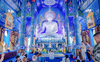 Interior of Blue Temple (Wat Rong Sua Ten) with white Buddha statue and ornate blue decor.