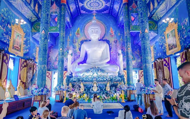 Interior of Blue Temple (Wat Rong Sua Ten) with white Buddha statue and ornate blue decor.