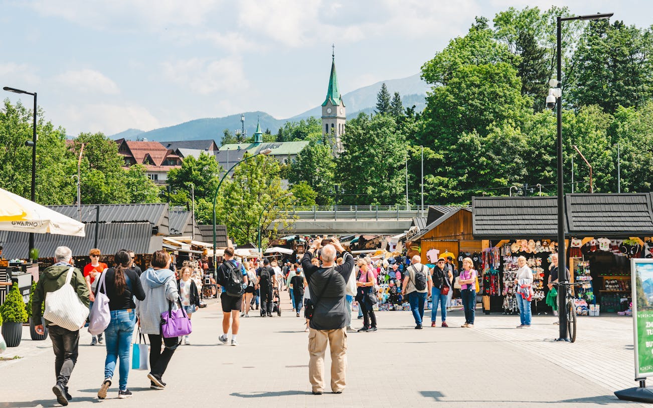 Zakopane market scene with tourists, local stalls, and a church tower in the background.