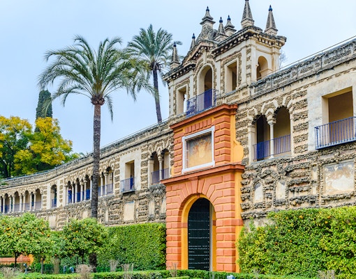 Mudéjar architecture of Alcazar Seville with ornate facade and lush gardens.